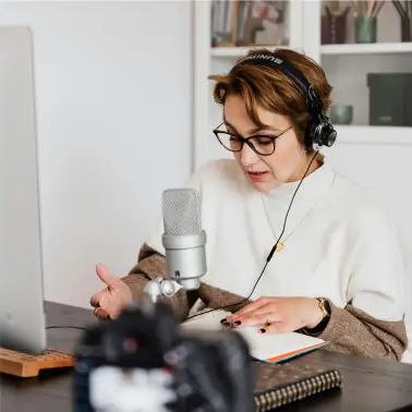 Une femme portant une chemise blanche et un pantalon noir est assise par terre et travaille sur son ordinateur portable dans un petit bureau situé dans une pièce confortable et bien éclairée.